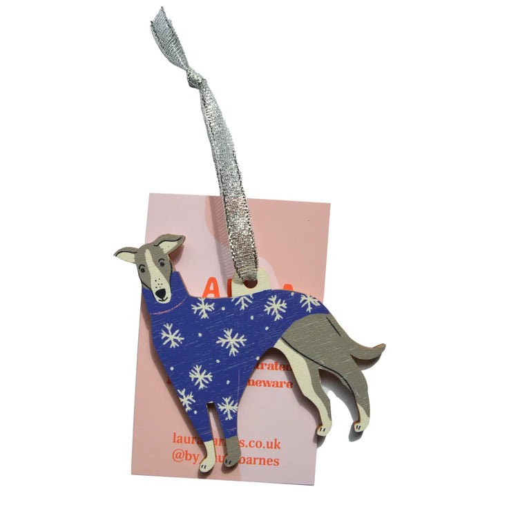 A wooden whippet hanging decoration with a tag card attached. They are wearing a blue and white snow decoration dog jacket.