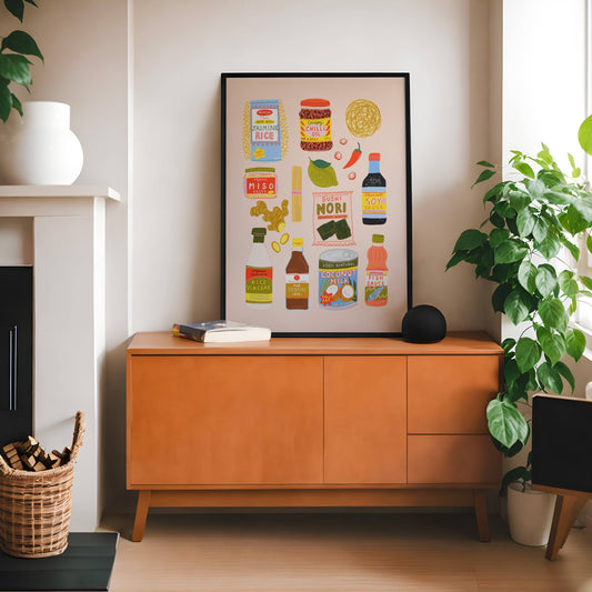 Wooden cabinet with a framed illustrated Asian food poster in a room with plants, a lamp and a just visible fireplace.